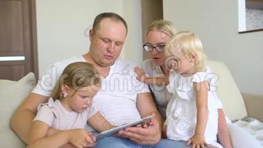 快乐的家庭<strong>一起玩</strong>笔记本电脑和数字<strong>平板</strong>电脑在家里。 爸爸，妈妈和两个孩子坐在沙发上